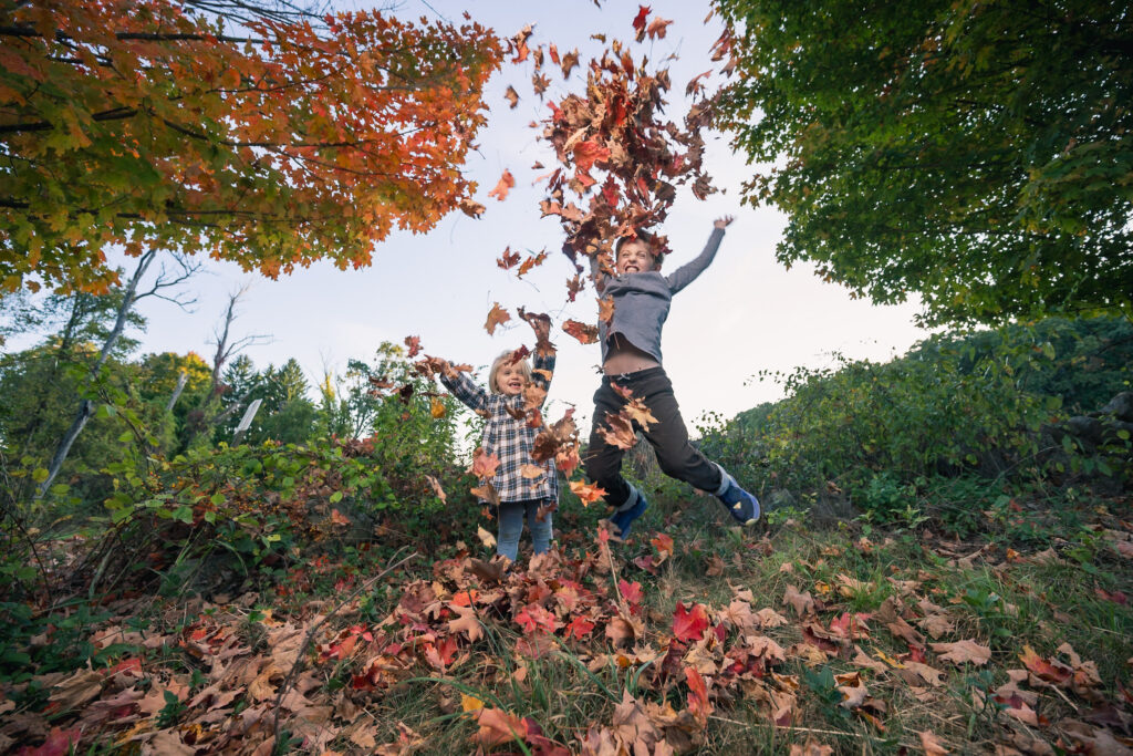 Two kids throw leaves in the air on a farm outside of Boston during a family photoshoot.