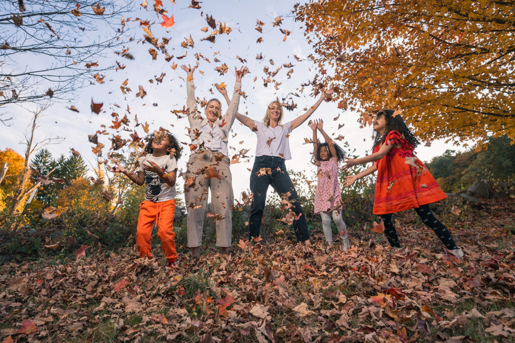 A joyful family playing and tossing autumn leaves in the air during a Fall family photo session at a farm in Lincoln, MA by Boston photographer Corey Flint.