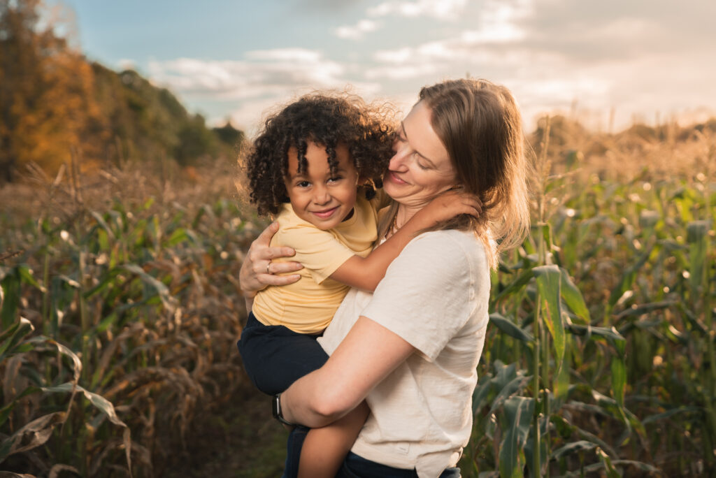 A mom holding her son in front of a field of corn on Flint Farm in Lincoln, Massachusetts.
