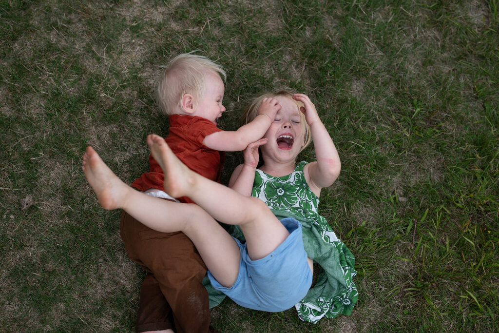 Two young children play on the grass, laughing and enjoying each other's company as they roll around.
