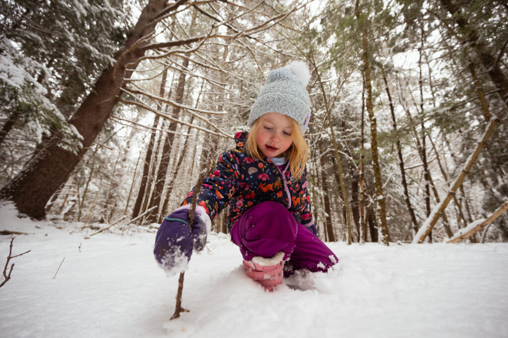 Girl sitting in snow looking up at sky during Boston area winter family photos session - Corey Flint Photography
