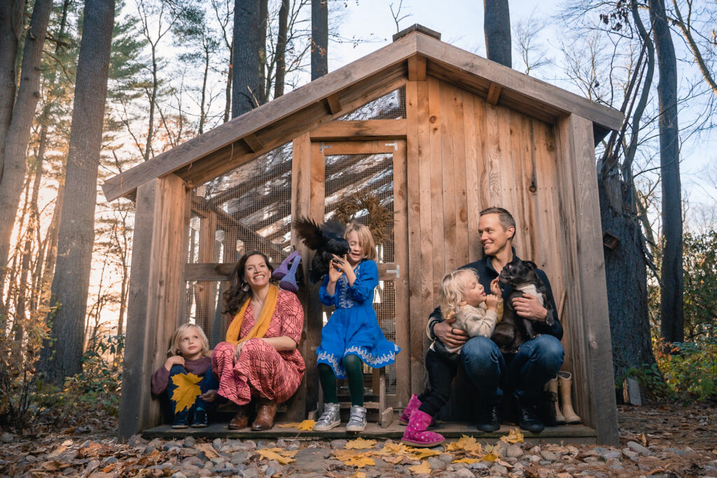 Family laughing at chicken coop with bird mid-flight in fall woods — documentary family photography by Corey Flint, Lincoln MA