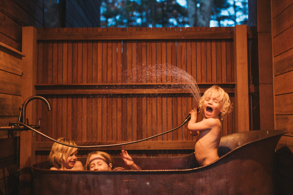 Three children playing in outdoor copper tub, one spraying water — candid family photography by Corey Flint, Lincoln Massachusetts