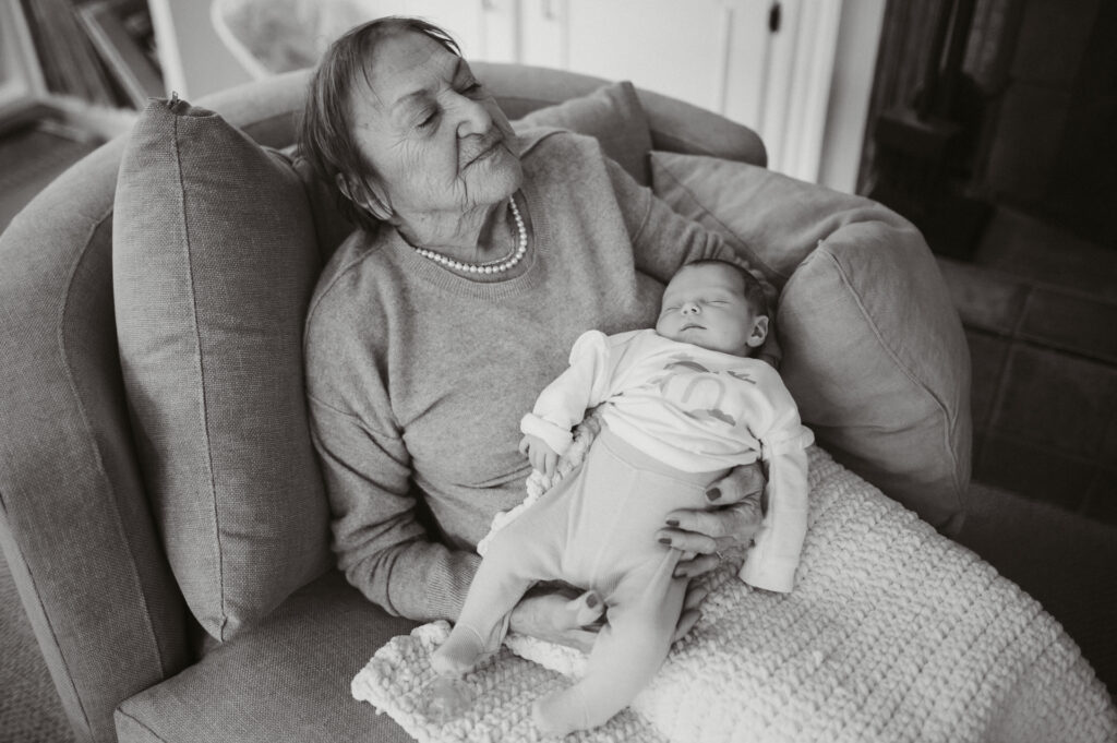 Black and white portrait of grandmother holding newborn in armchair — family photographer Corey Flint, Lincoln Massachusetts