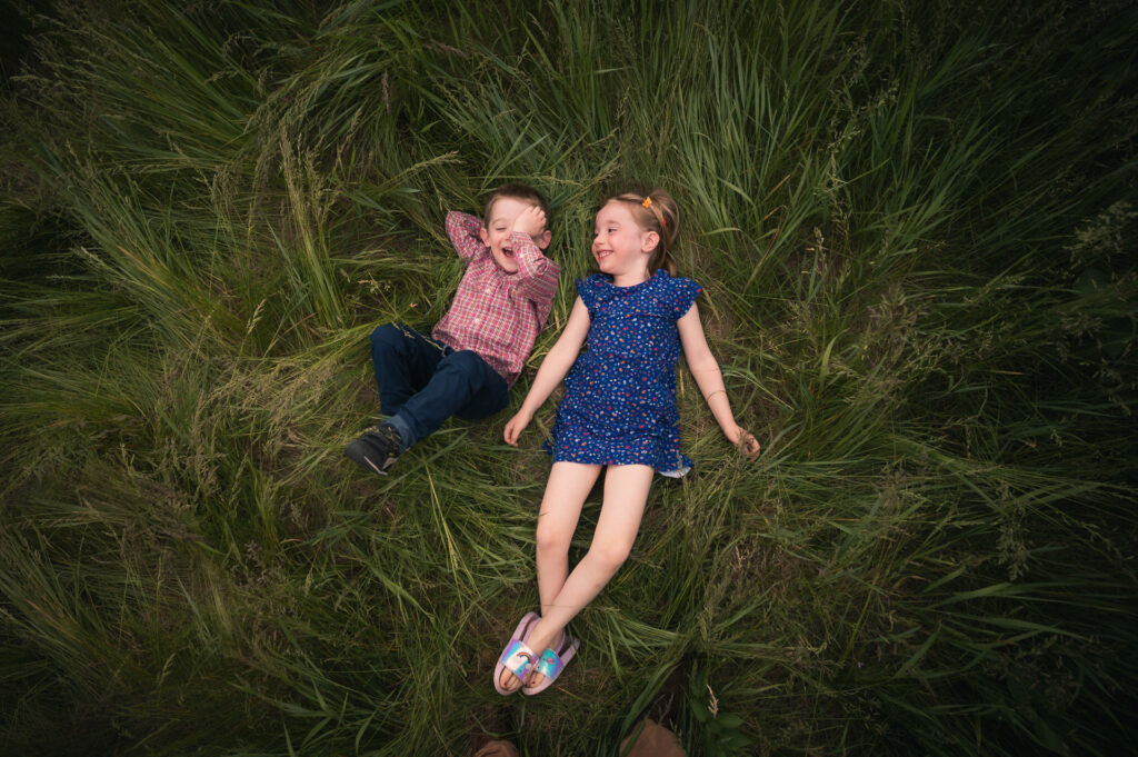 Two siblings laughing while lying in tall grass, photographed from directly above — Corey Flint Photography, Lincoln MA
