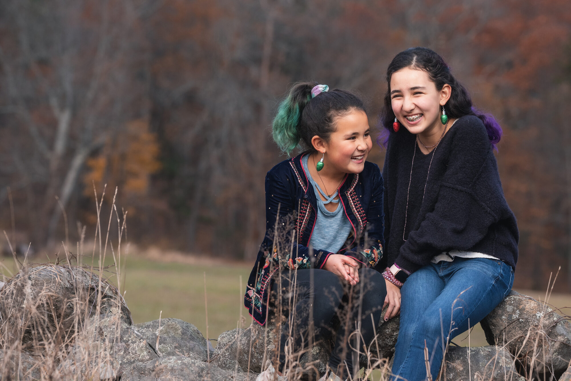 Two sisters laughing together on a stone wall during their annual fall family session