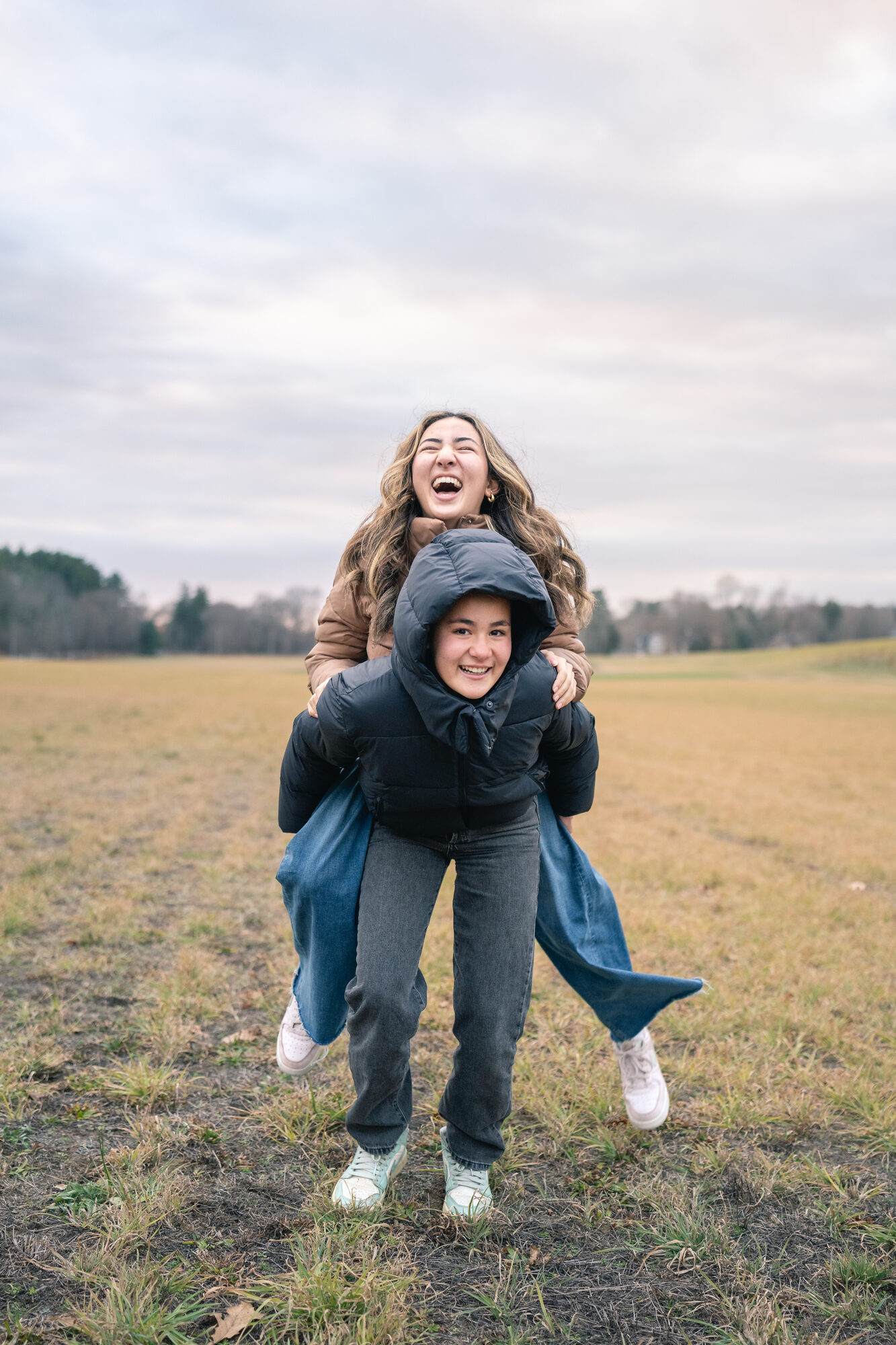 One sister giving the other a piggyback ride and laughing in an open field