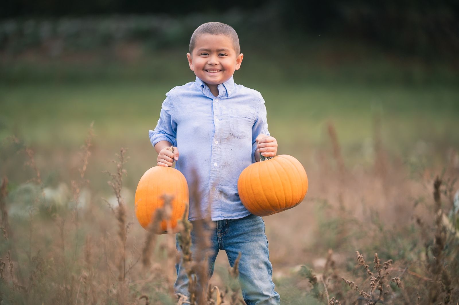 A smiling boy carrying a pumpkin in each hand in the Flint Farm pumpkin patch in Lincoln, MA