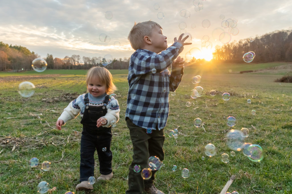 kids wearing plaid and overalls chasing bubbles at sunset 